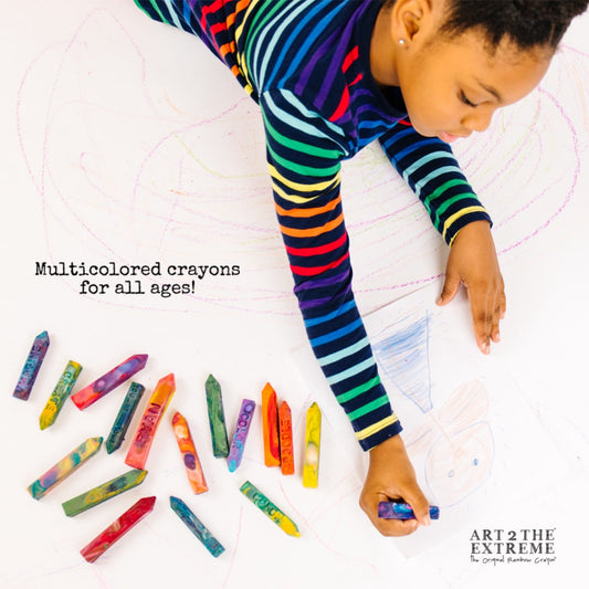Child holding a rainbow Crayon Stix® from Art 2 the Extreme coloring on a white floor and white paper. Text that reads Multicolored crayons for all ages. 