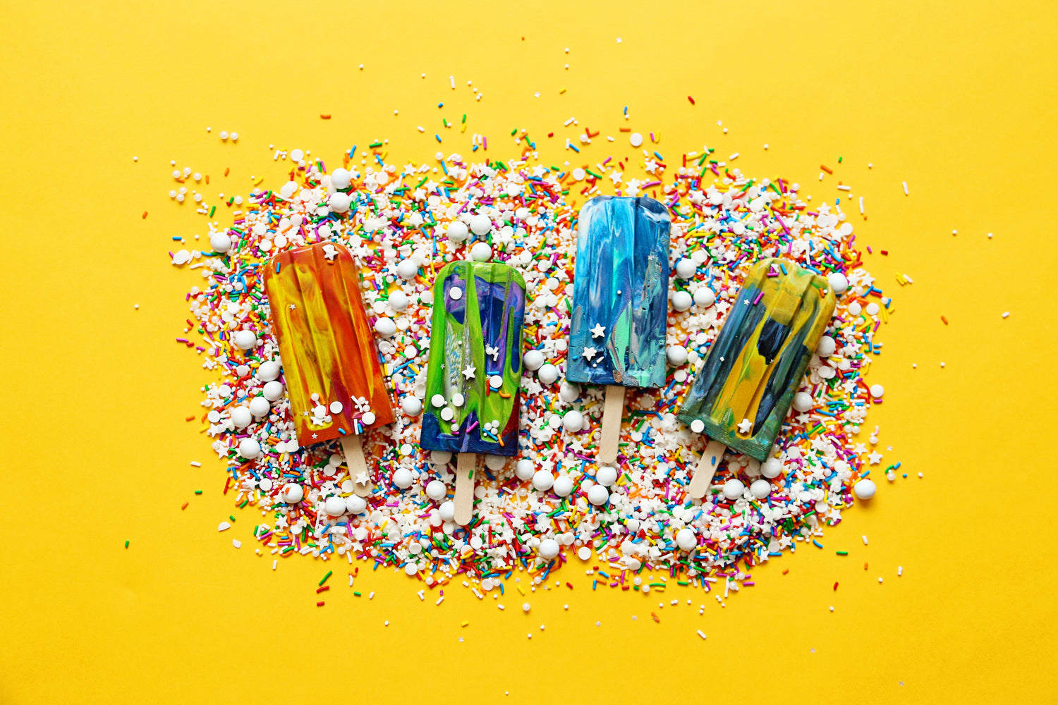 Popsicle crayon party favors from rainbow crayon shop Art 2 the Extreme, home of the Original Rainbow Crayon®. Image is 4 popsicle crayons on a yellow background with sprinkles as summer party favor ideas for kids. 