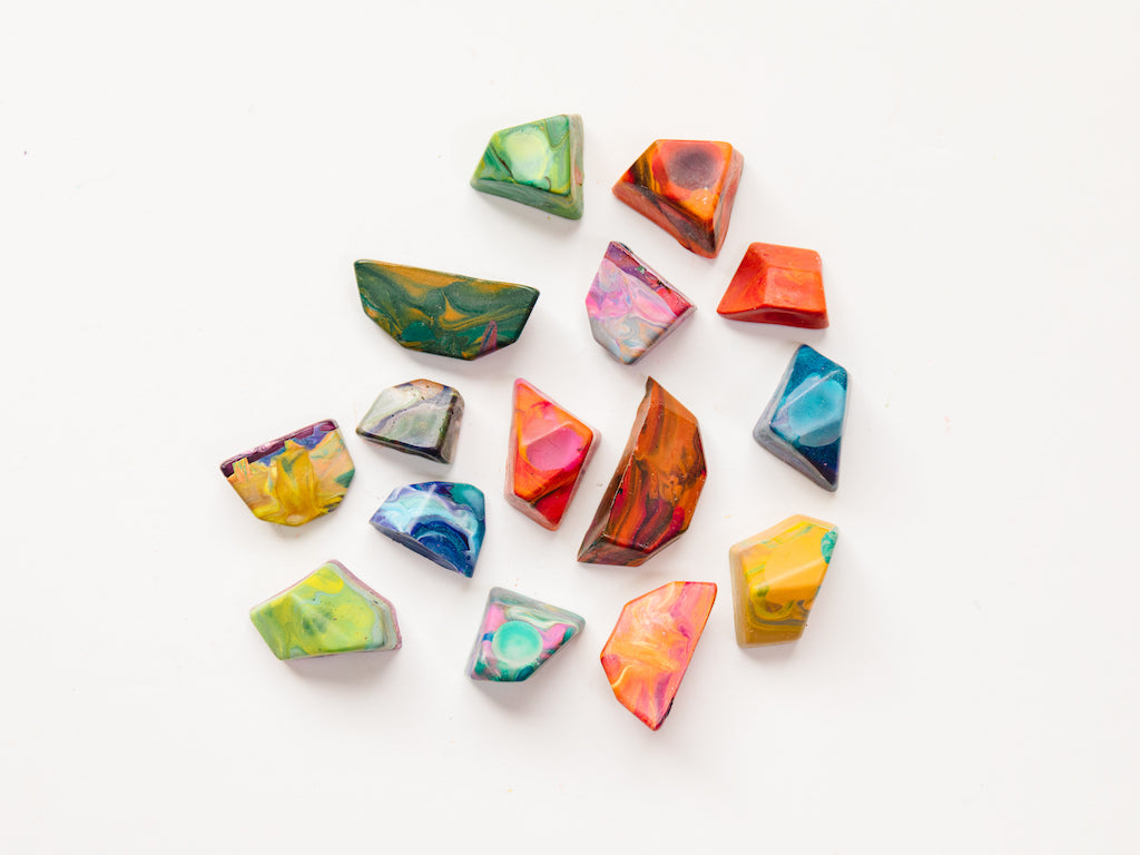 15 multi-colored rainbow rock crayons on a white background. Each crayon rock is shown in a variety of swirly hues that will color  with multiple colors when used on a paper.  Rocks are mini size and measure about 1-2" in length or width and 1/2" -1" in height. Size varies and the edges are very angular for crayons, making this a great gift for younger kids just learning to hold a crayon. 